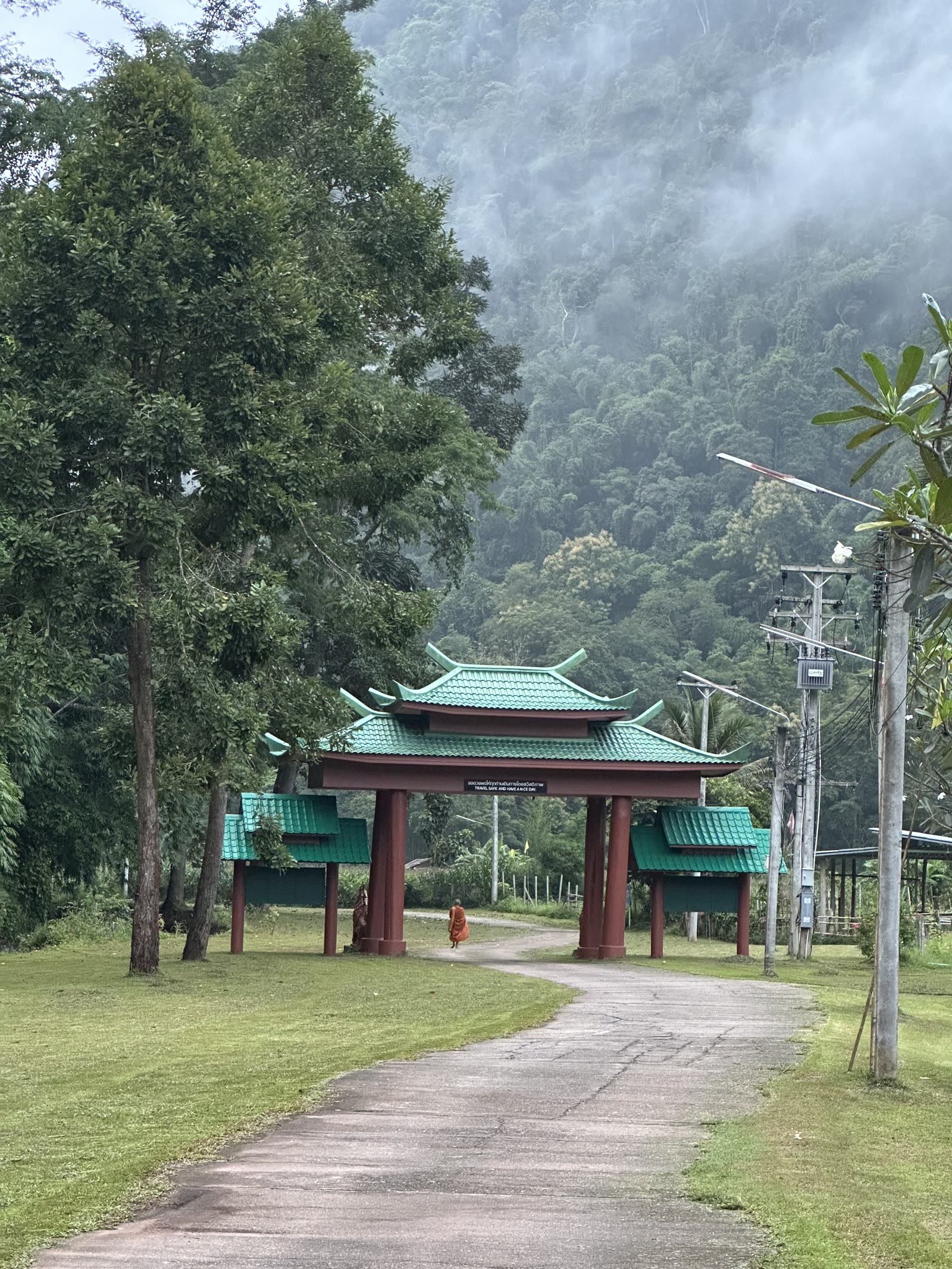 Entrance gate at Wat Pa Tam Wua with a monk walking through and mist on the mountain behind